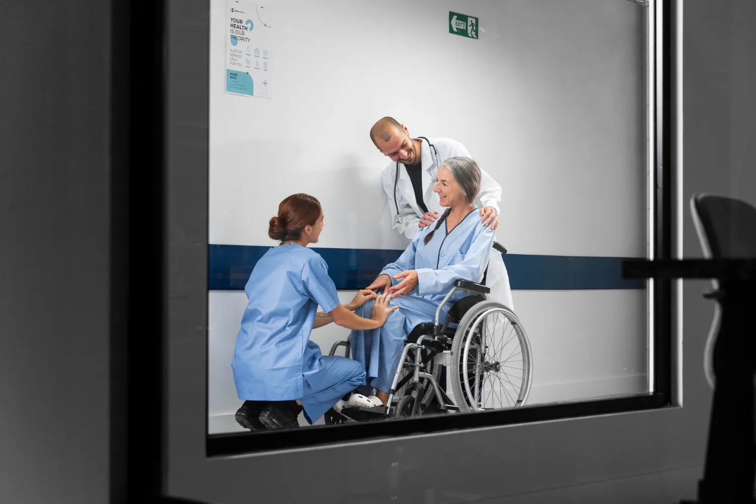 Two healthcare professionals assist a patient in a wheelchair in a hospital hallway, conveying care and support